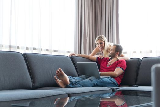 Young couple using laptop computer at luxury home together, looking at screen, smiling.