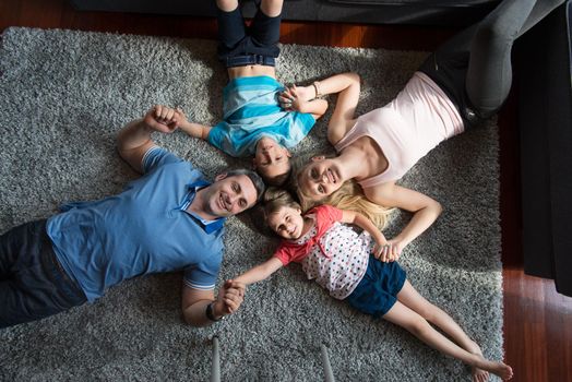 Top view of beautiful young parents, their cute little daughter and son holding hands, looking at camera and smiling, lying on the floor