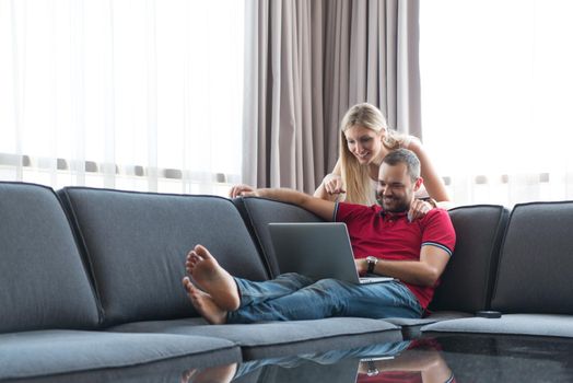 Young couple using laptop computer at luxury home together, looking at screen, smiling.