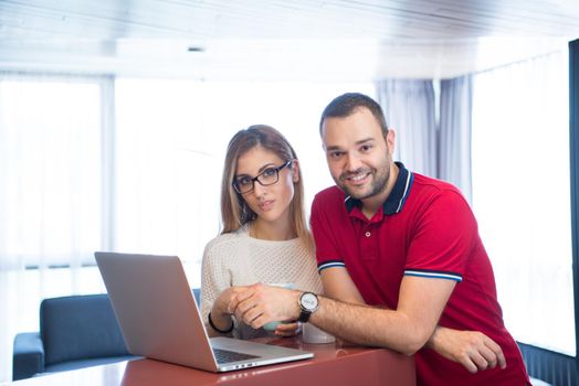 Young couple drinking coffee and using laptop computer at luxury home together, looking at screen, smiling.