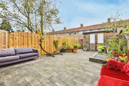 Cozy courtyard of a house with pots of flowers and a bright scarlet velvet sofa