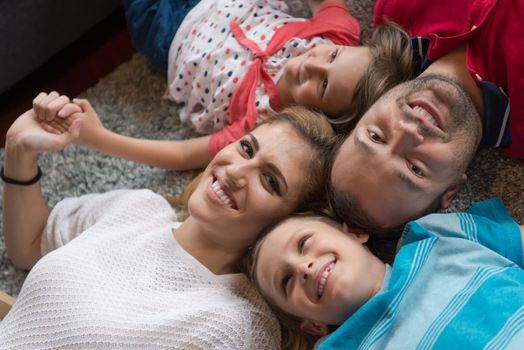 Top view of beautiful young parents, their cute little daughter and son holding hands, looking at camera and smiling, lying on the floor