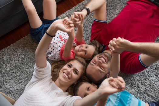 Top view of beautiful young parents, their cute little daughter and son holding hands, looking at camera and smiling, lying on the floor