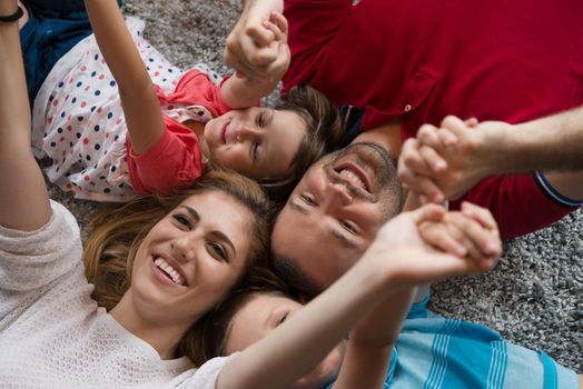 Top view of beautiful young parents, their cute little daughter and son holding hands, looking at camera and smiling, lying on the floor