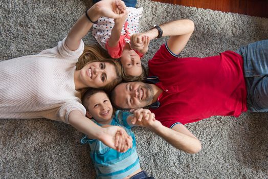 Top view of beautiful young parents, their cute little daughter and son holding hands, looking at camera and smiling, lying on the floor