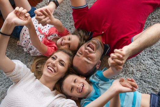 Top view of beautiful young parents, their cute little daughter and son holding hands, looking at camera and smiling, lying on the floor