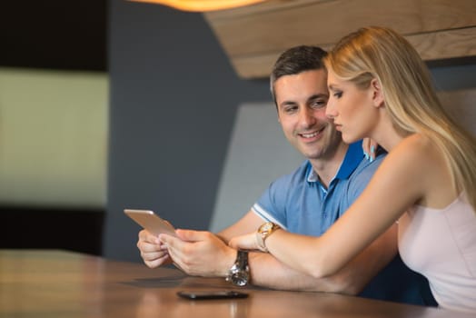 Young couple using tablet computer at luxury home together, looking at screen, smiling.