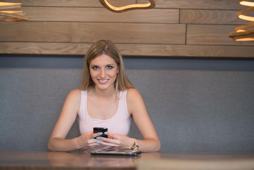 young happy woman sitting at the table and using mobile phone at luxury home