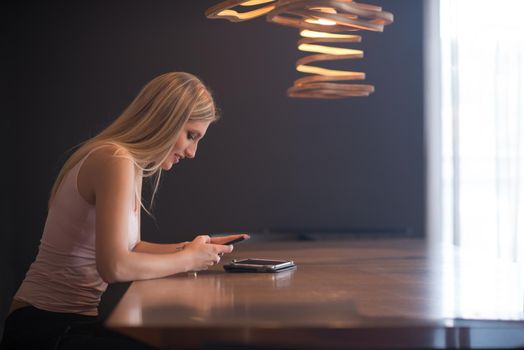 young happy woman sitting at the table and using mobile phone at luxury home