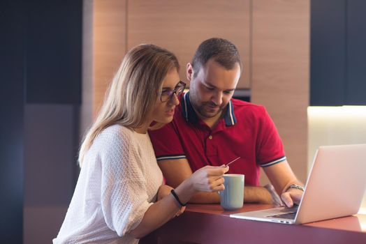 happy young couple buying online using laptop a computer and a credit card in their luxury home villa