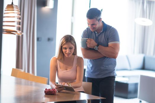 Young couple using tablet computer at luxury home together, looking at screen, smiling.