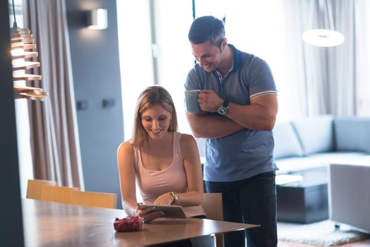 Young couple using tablet computer at luxury home together, looking at screen, smiling.