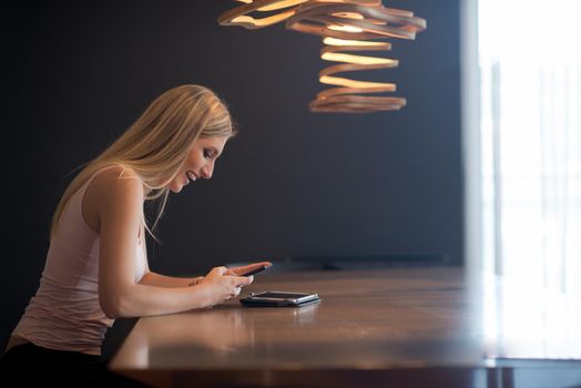 young happy woman sitting at the table and using mobile phone at luxury home