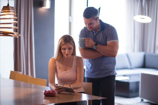 Young couple using tablet computer at luxury home together, looking at screen, smiling.