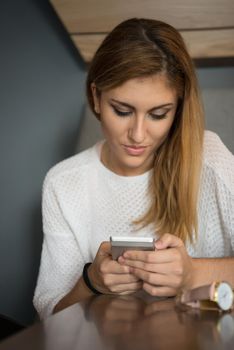 young happy woman sitting at the table and using mobile phone at luxury home