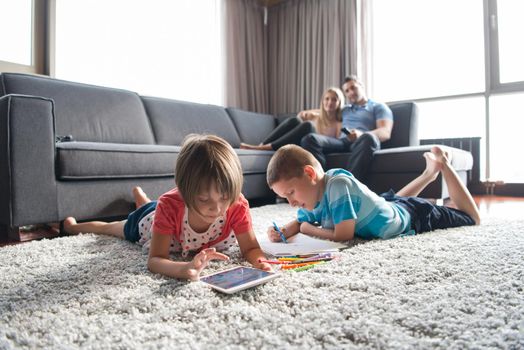 Happy Young Family Playing Together at home on the floor using a tablet and a children's drawing set