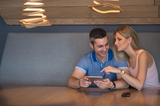 Young couple using tablet computer at luxury home together, looking at screen, smiling.