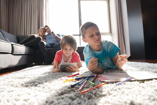 Happy Young Family Playing Together at home on the floor using a tablet and a children's drawing set