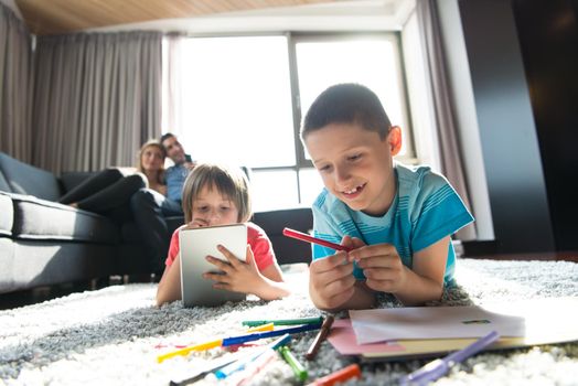 Happy Young Family Playing Together at home on the floor using a tablet and a children's drawing set