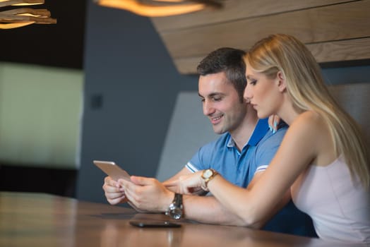 Young couple using tablet computer at luxury home together, looking at screen, smiling.