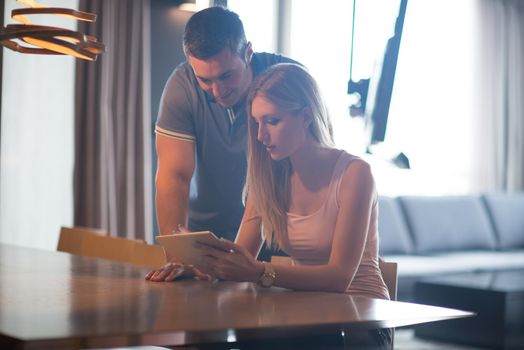 Young couple using tablet computer at luxury home together, looking at screen, smiling.