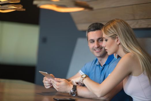 Young couple using tablet computer at luxury home together, looking at screen, smiling.