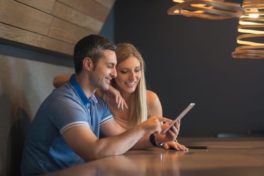 Young couple using tablet computer at luxury home together, looking at screen, smiling.