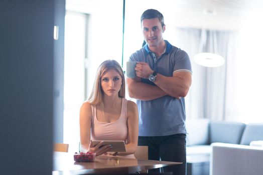 Young couple using tablet computer at luxury home together, looking at screen, smiling.