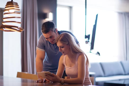 Young couple using tablet computer at luxury home together, looking at screen, smiling.