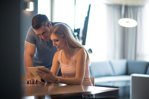 Young couple using tablet computer at luxury home together, looking at screen, smiling.