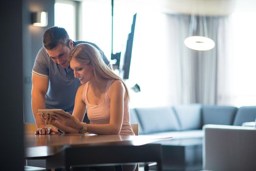 Young couple using tablet computer at luxury home together, looking at screen, smiling.