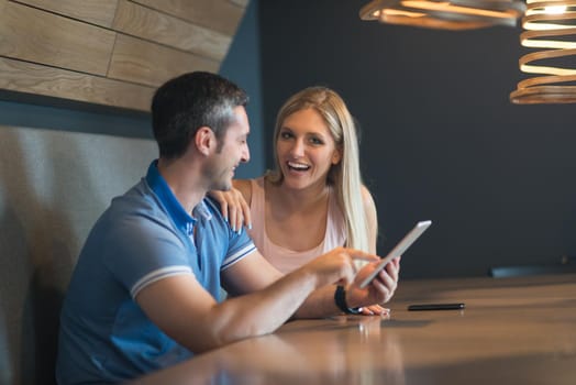 Young couple using tablet computer at luxury home together, looking at screen, smiling.