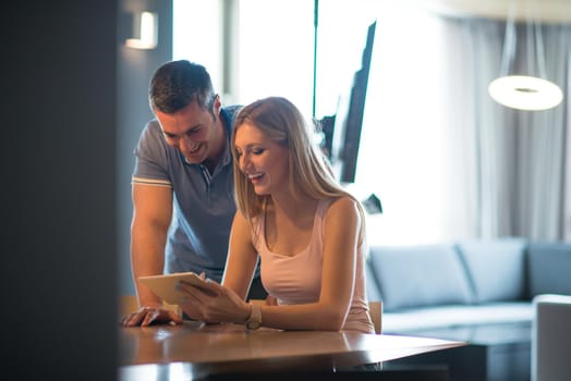 Young couple using tablet computer at luxury home together, looking at screen, smiling.