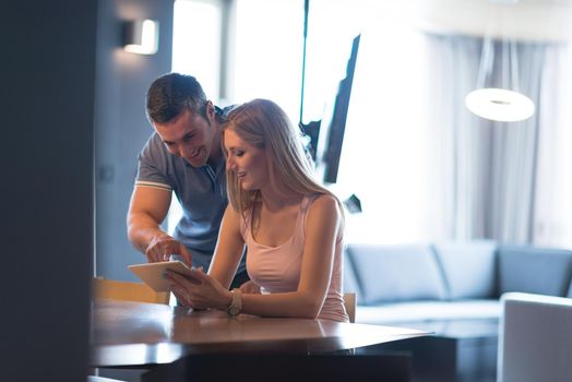 Young couple using tablet computer at luxury home together, looking at screen, smiling.