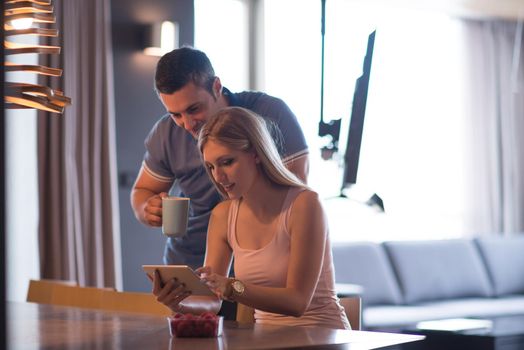 Young couple using tablet computer at luxury home together, looking at screen, smiling.