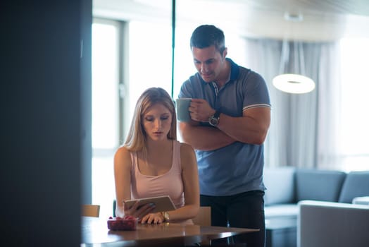 Young couple using tablet computer at luxury home together, looking at screen, smiling.