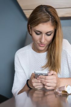 young happy woman sitting at the table and using mobile phone at luxury home