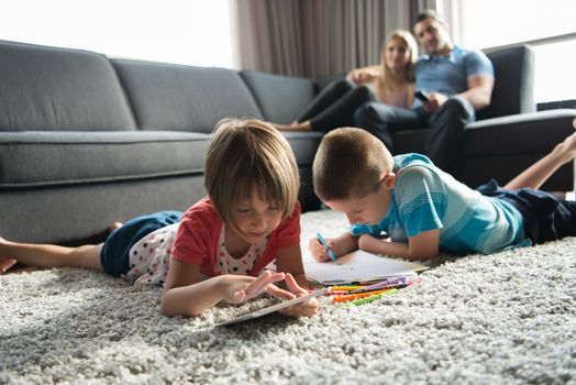 Happy Young Family Playing Together at home on the floor using a tablet and a children's drawing set