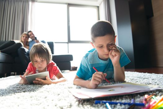 Happy Young Family Playing Together at home on the floor using a tablet and a children's drawing set