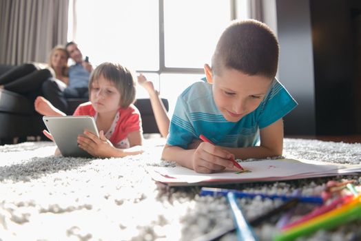 Happy Young Family Playing Together at home on the floor using a tablet and a children's drawing set