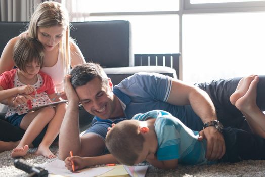 Happy Young Family Playing Together at home on the floor using a tablet and a children's drawing set