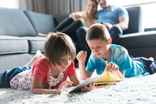 Happy Young Family Playing Together at home on the floor using a tablet and a children's drawing set