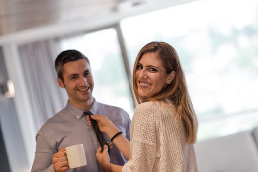 A young couple is preparing for the job and using a laptop. The man drinks coffee while the woman eats breakfast at luxury home together, looking at screen, smiling.