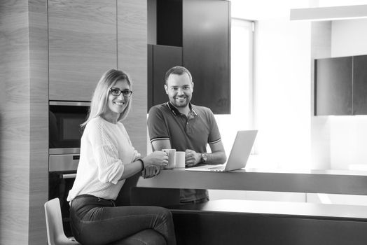 Young couple drinking coffee and using laptop computer at luxury home together, looking at screen, smiling.