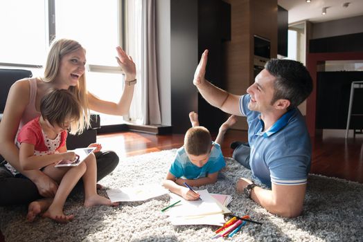 Happy Young Family Playing Together at home on the floor using a tablet and a children's drawing set