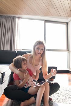 Beautiful young mother and her cute little daughter  using a tablet and smiling, sitting on the floor at home