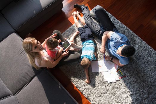Happy Young Family Playing Together at home on the floor using a tablet and a children's drawing set top view