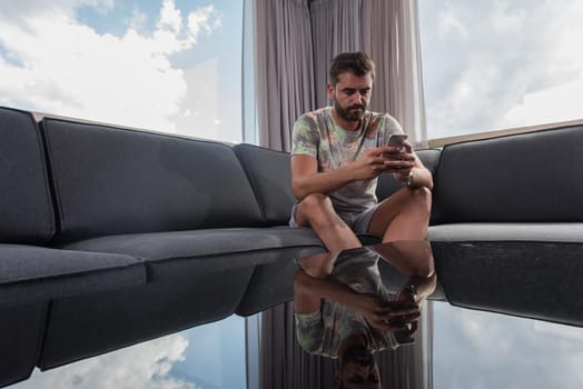 young man sitting on sofa and using a mobile phone  near the window at home