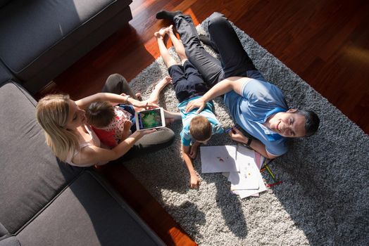 Happy Young Family Playing Together at home on the floor using a tablet and a children's drawing set top view