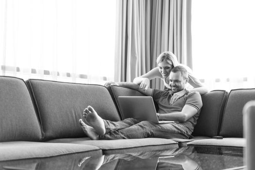 Young couple using laptop computer at luxury home together, looking at screen, smiling.